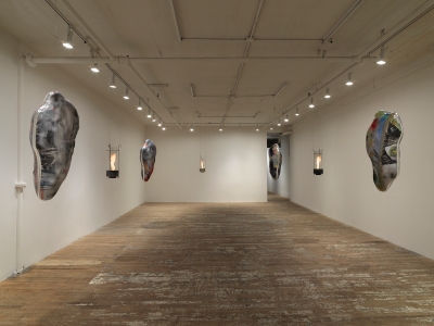 A gallery with cocoon-like sculptures and sculptures holding live flames hanging in its center.