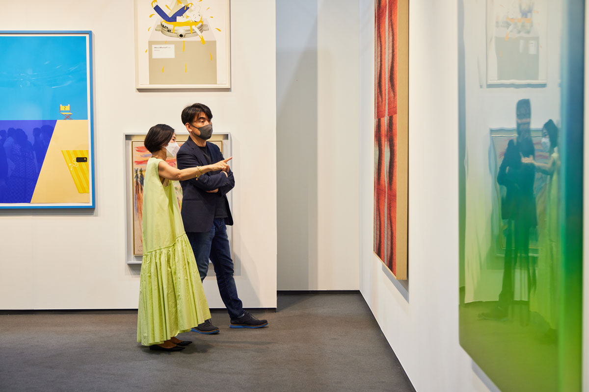 Two people stand in an art fair looking at an artwork.
