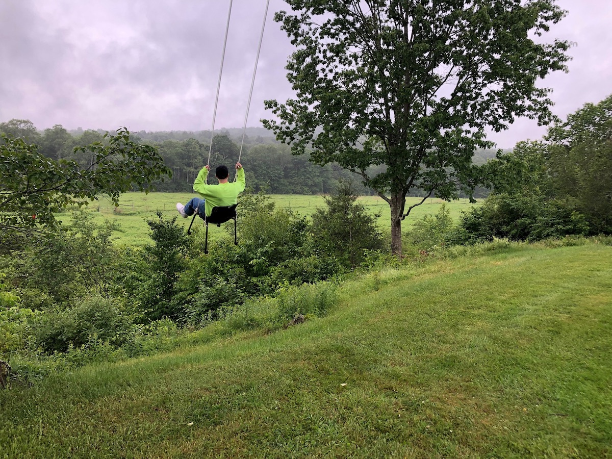 A person in a swing above a grassy hill that looks out onto mountains.