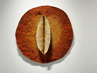 A sculptural work in ochre and yellow or a circle with at its center two lips that resemble a vagina.