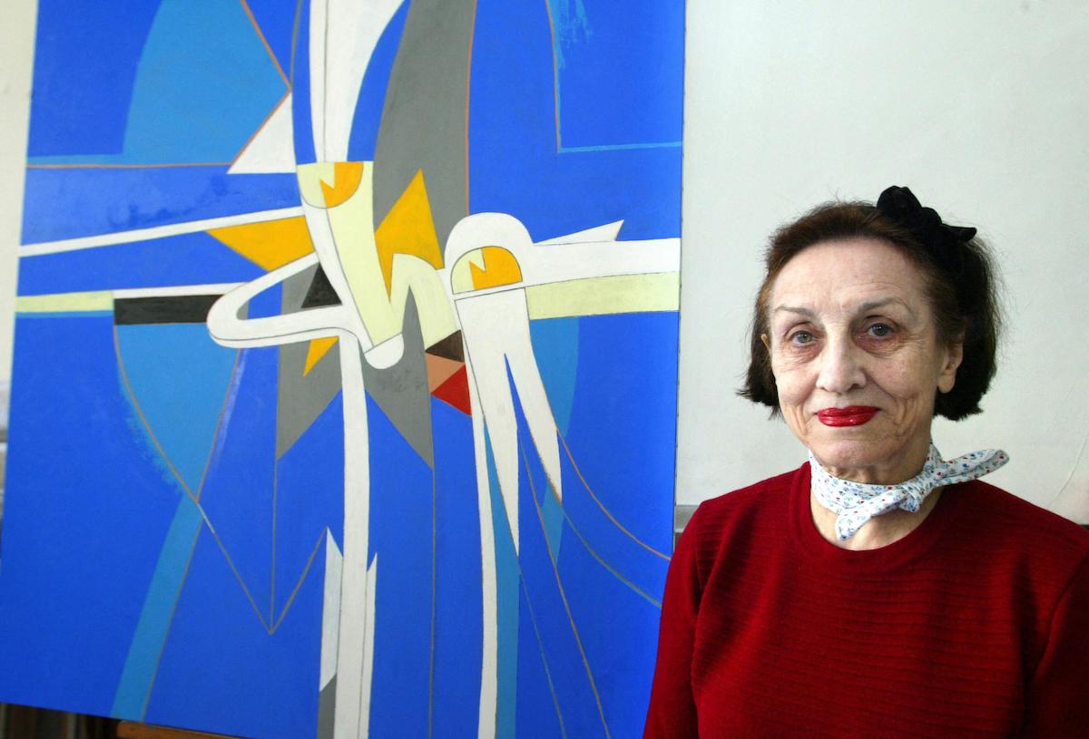 A woman standing beside a bright blue abstract painting.