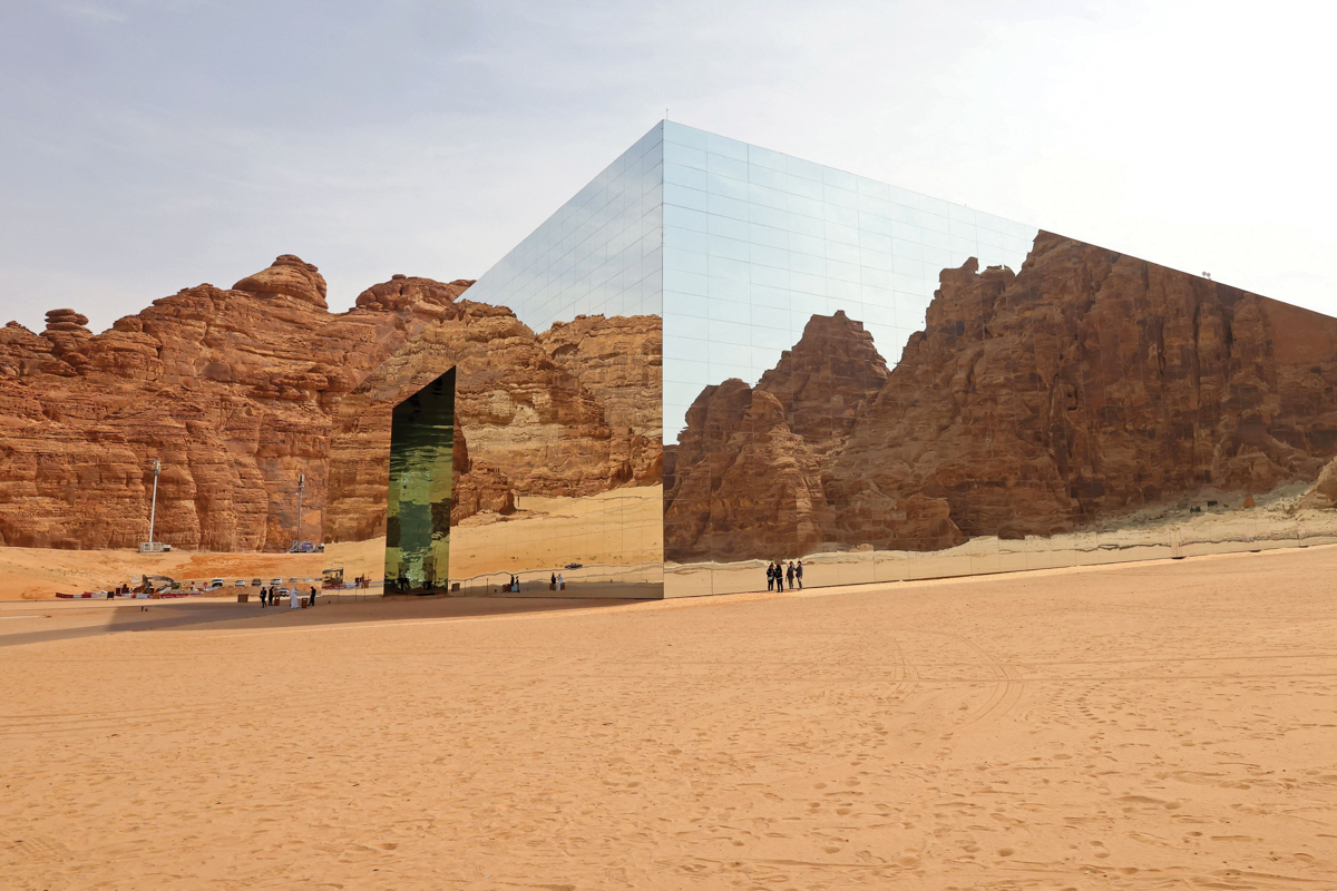 A mirrored rectangular building reflects a desert landscape.