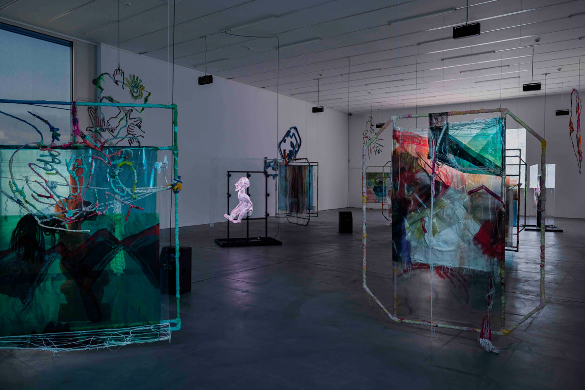Installation view of a museum exhibition showing various sculptural works suspended from the ceiling. 