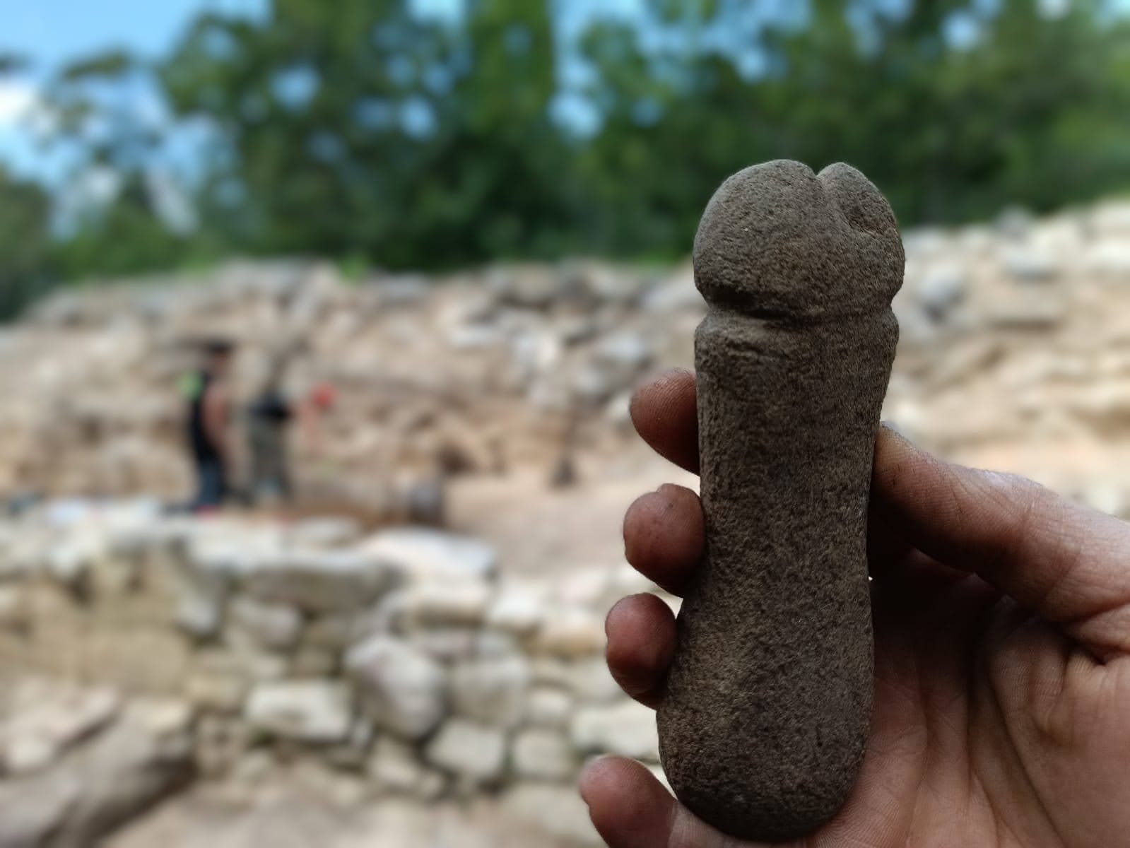 A hand holds a stone, penis-shaped object.