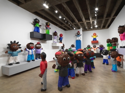 A gallery filled with numerous piñatas resembling Black men with their hands extended outward.