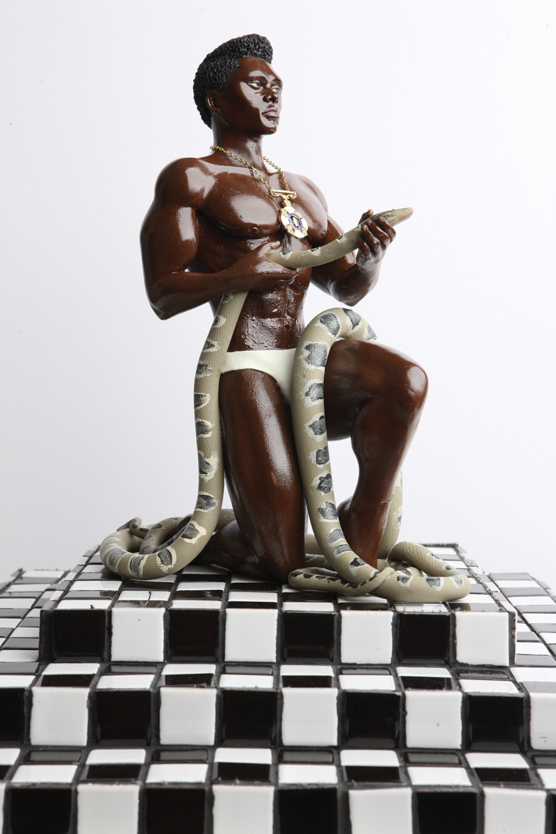 A sculpture of a Black man in white underwear holding a giant snake, on a checkered pedestal.