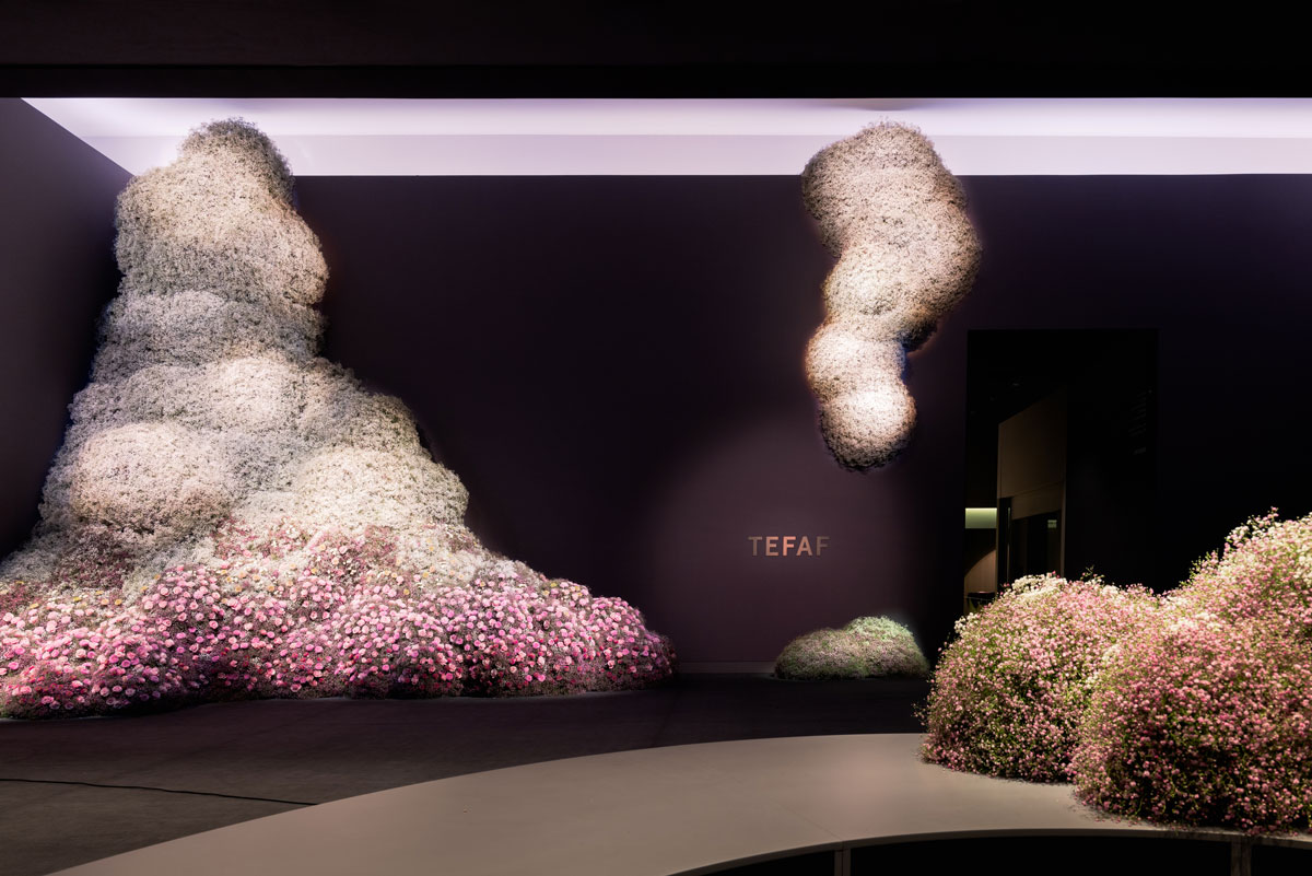 Several sculptural works made by flowers hang in an eggplant-painted room with TEFAF logo visible in the center.